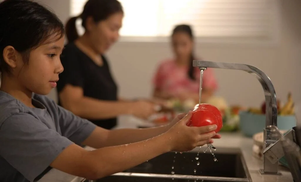 Un niño lava un pimiento rojo bajo el grifo de la cocina