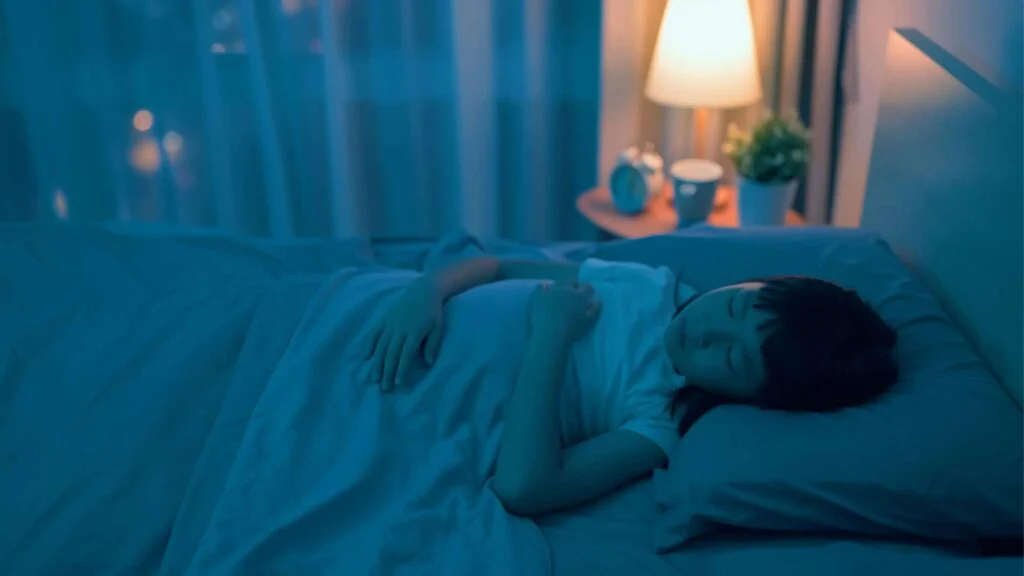 Niña asiática durmiendo en su cama con una luz nocturna encendida