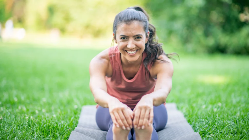 Una mujer estirándose en un mat de yoga al aire libre practicando recuperación activa