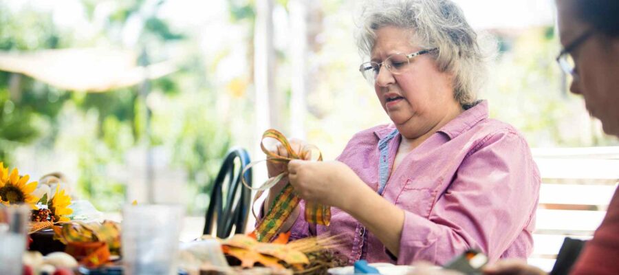 Mujer mayor haciendo manualidades en una mesa con amigos