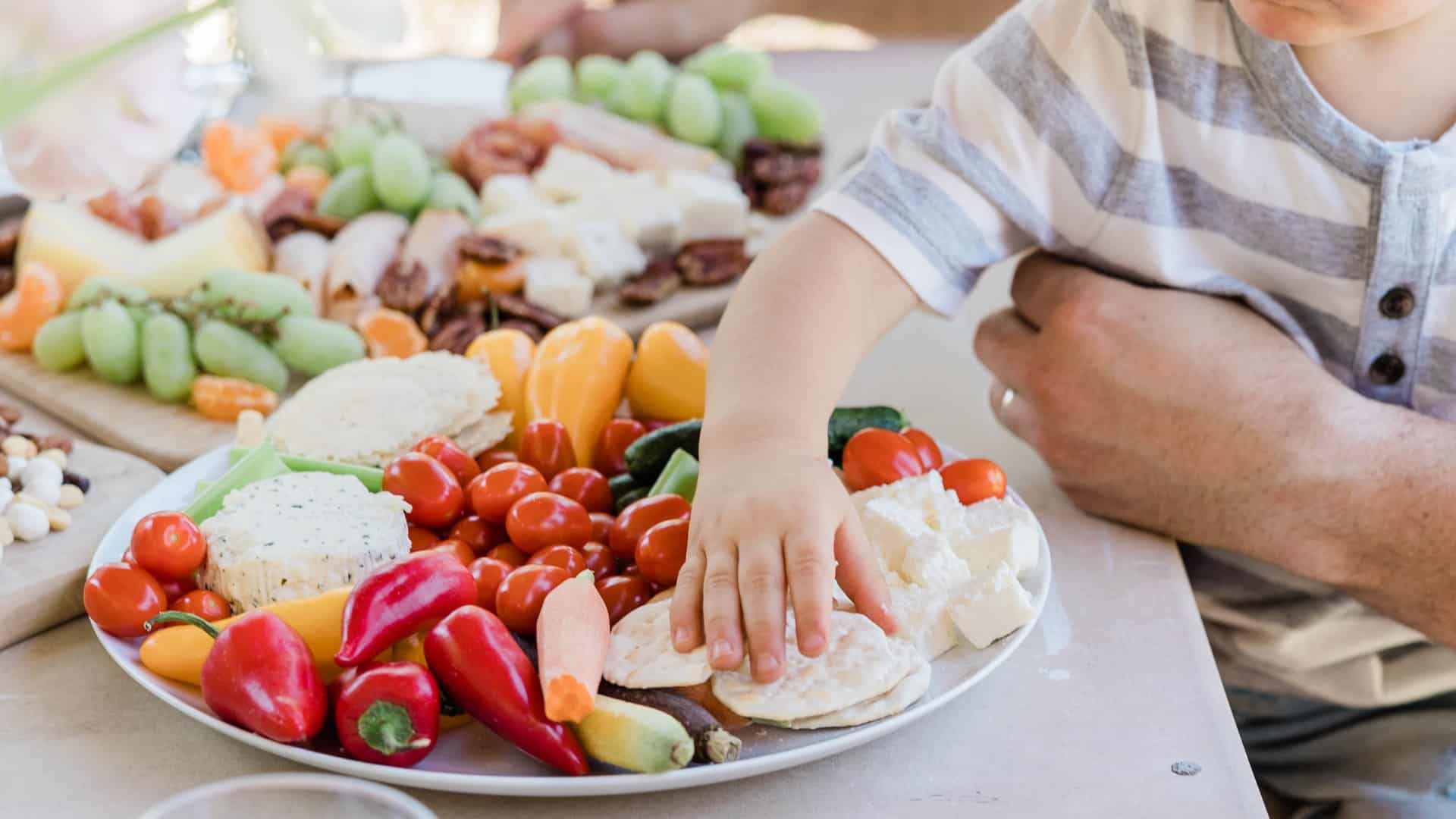 Un niño pequeño alcanza una galleta en un plato de verduras
