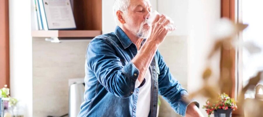 Hombre mayor bebiendo un vaso de agua en su cocina