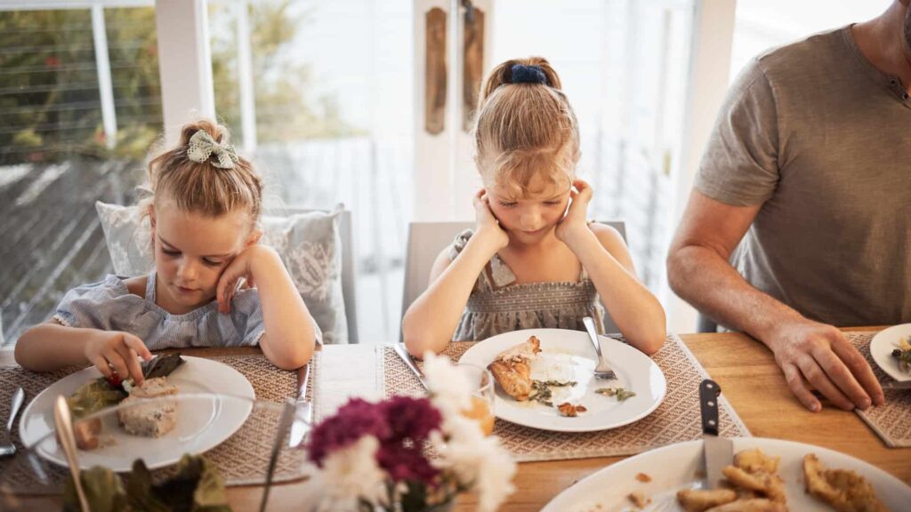 Dos niñas sentadas en la mesa mirando la cena en su plato